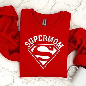 May include: Red sweatshirt with a white Superman logo and the text "SUPERMOM" printed on the front.
