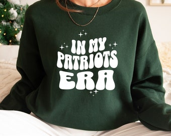 May include: A dark green sweatshirt with white text that reads "In My Patriots Era" in a retro font. The text is surrounded by small white stars.
