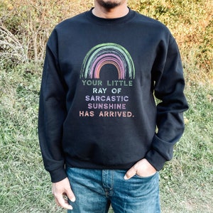 May include: Black sweatshirt with a rainbow graphic and the text "Your little ray of sarcastic sunshine has arrived."