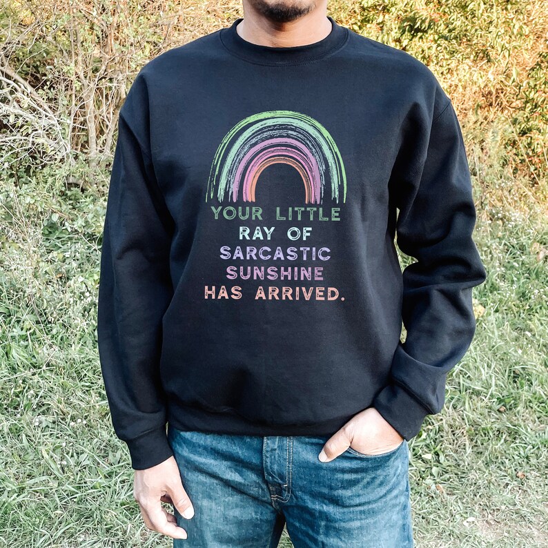 May include: Black sweatshirt with a rainbow graphic and the text "Your little ray of sarcastic sunshine has arrived."