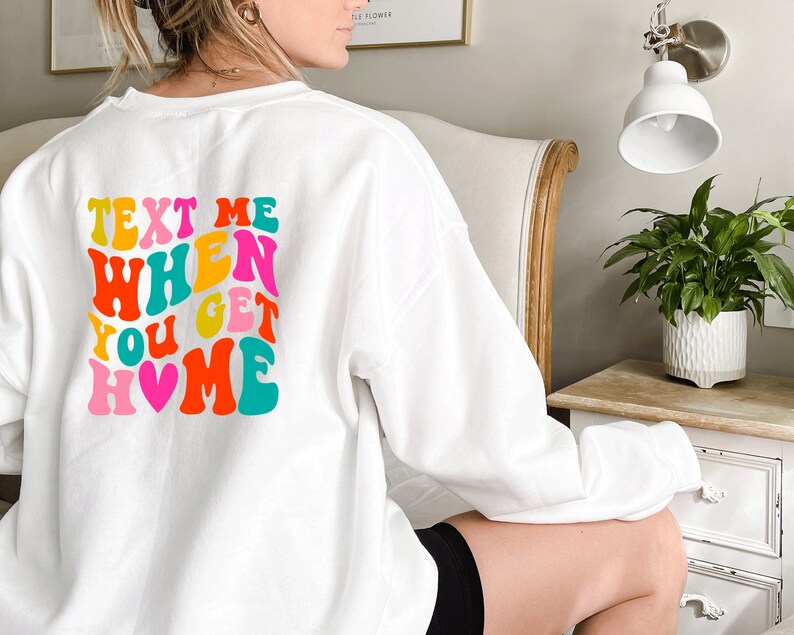 May include: White sweatshirt with a colourful retro-style graphic that says "Text Me When You Get Home" with a pink heart.