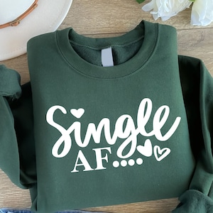May include: A dark green sweatshirt with the text "Single AF..." in white with small heart graphics.