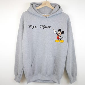 Peut inclure: Sweat-shirt &agrave; capuche gris avec le texte "Mrs. Miller" et une image de dessin anim&eacute; de Mickey Mouse tenant un pointeur.