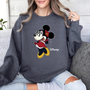 May include: A dark gray sweatshirt with a cartoon image of Minnie Mouse in a red dress and yellow shoes. The text "Disney" is printed below the image.