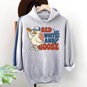 May include: A light gray hooded sweatshirt featuring a cartoon goose wearing a hat that says "Merica" and holding a hot dog. The text "Red, White, and Goose" is printed in red, white, and blue. The sweatshirt has a front pocket.