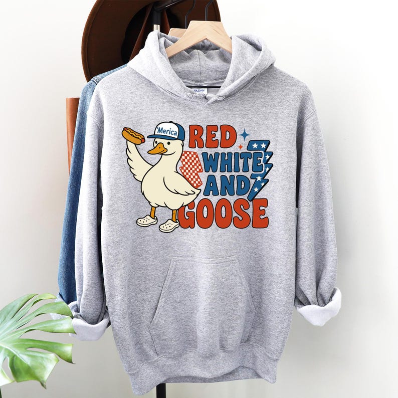 May include: A light gray hooded sweatshirt featuring a cartoon goose wearing a hat that says "Merica" and holding a hot dog. The text "Red, White, and Goose" is printed in red, white, and blue. The sweatshirt has a front pocket.