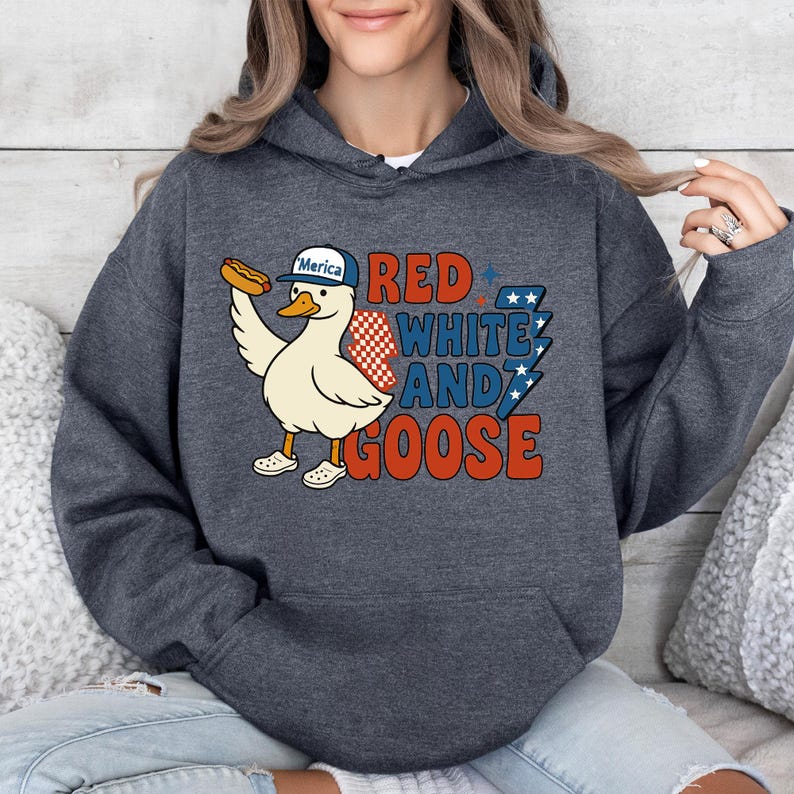 May include: Dark gray hoodie featuring a cartoon goose wearing a baseball cap that says "Merica" and holding a hot dog. The text "Red, White, and Goose" is printed in red, white, and blue. The hoodie is a comfortable, casual style.