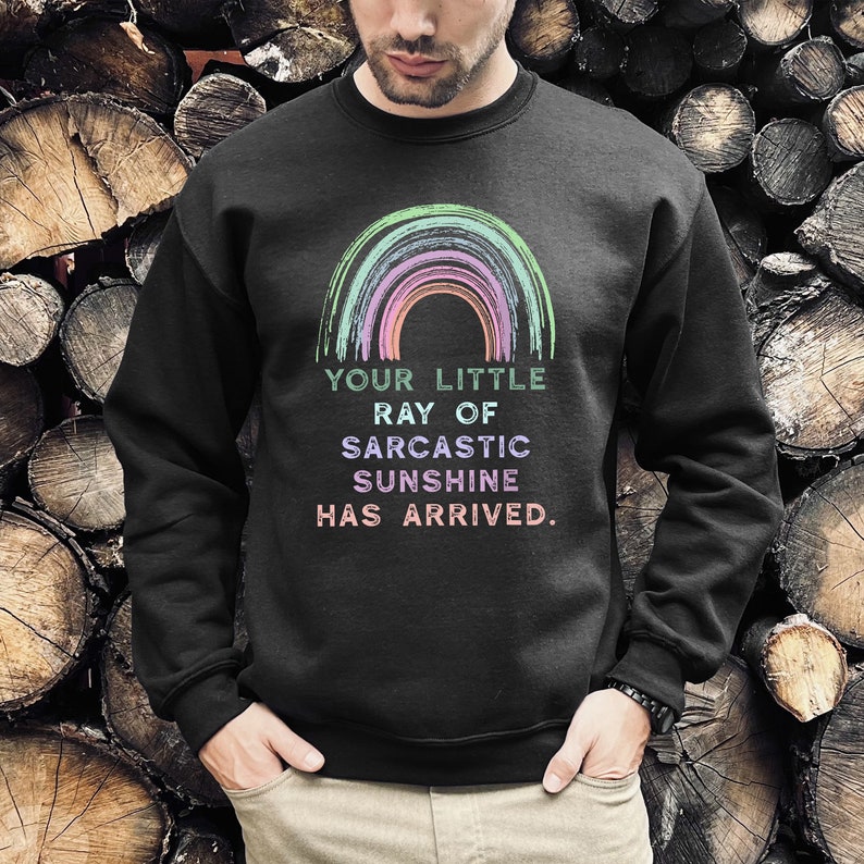 May include: A black sweatshirt with a rainbow graphic and the text "Your little ray of sarcastic sunshine has arrived."