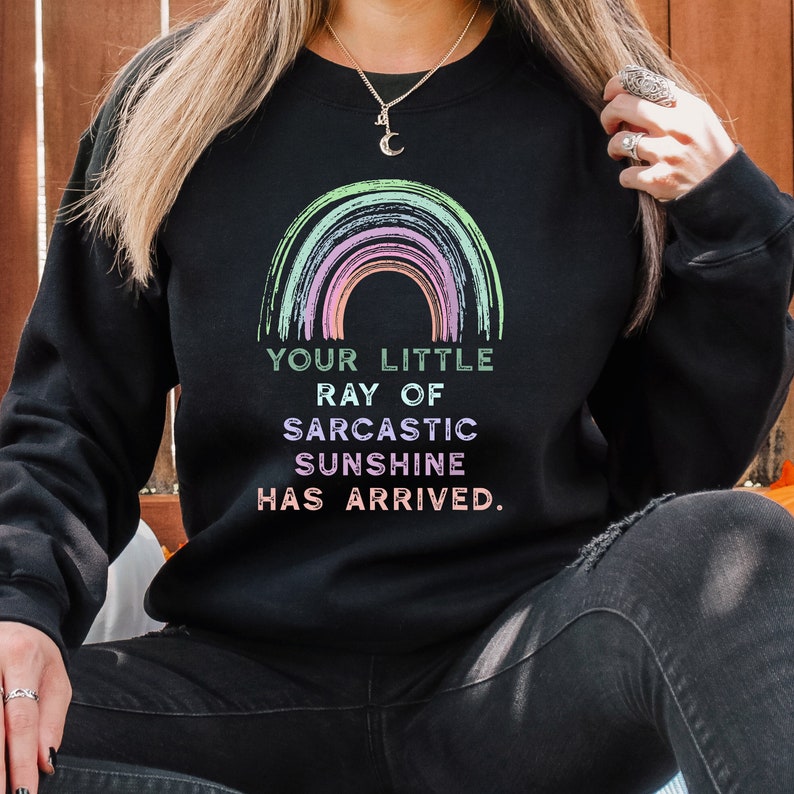 May include: Black sweatshirt with a rainbow graphic and the text "Your little ray of sarcastic sunshine has arrived."