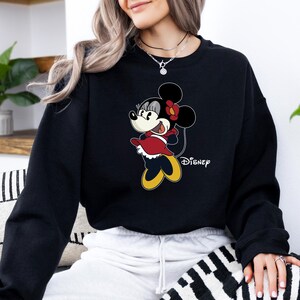 May include: Black sweatshirt with a cartoon image of Minnie Mouse wearing a red dress and a yellow bow. The text "DISNEY" is printed on the bottom right corner of the sweatshirt.