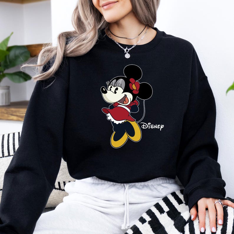 May include: Black sweatshirt with a cartoon image of Minnie Mouse wearing a red dress and a yellow bow. The text "DISNEY" is printed on the bottom right corner of the sweatshirt.