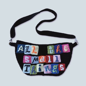 May include: A black crocheted bag with a shoulder strap. The bag has a colorful crocheted design that says "All the small things".