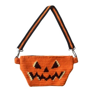 May include: An orange crocheted pumpkin-shaped crossbody bag with a black and orange strap. The bag has a black crocheted jack-o'-lantern face.