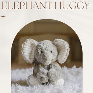 May include: A gray plush elephant toy with a white fabric texture on the ears and feet. The elephant is sitting on a white fluffy rug. The text "ELEPHANT HUGGY" is at the top of the image and "WWW.HUGGYHYMNS.COM" is at the bottom.