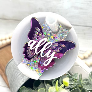 May include: A purple butterfly-shaped diffuser charm with iridescent glitter and the name "ally" written in white.