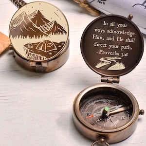 May include: A vintage-style compass with a bronze finish. The lid features an engraved mountain and tent scene. The open compass reveals a directional dial. The inside lid has the text: "In all your ways acknowledge Him, and He shall direct your path. -Proverbs 3:6."