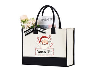 Peut inclure: Un sac fourre-tout blanc avec des poignées noires et une base noire. Il présente un motif de Père Noël avec des cannes en bonbon et le texte "Custom Text". Le sac contient des fleurs et un magazine.