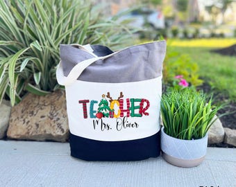 May include: A grey and white tote bag with a Christmas-themed "Teacher" design and the text "Mrs. Oliver".