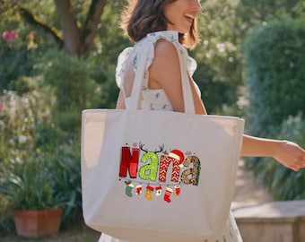 Peut inclure: Un sac fourre-tout en toile blanche avec le mot "Nana" dans un design festif et coloré. Les lettres sont décorées de motifs de Noël, dont du tartan, des bois de rennes et un bonnet de Père Noël. En dessous, des chaussettes de Noël suspendues.