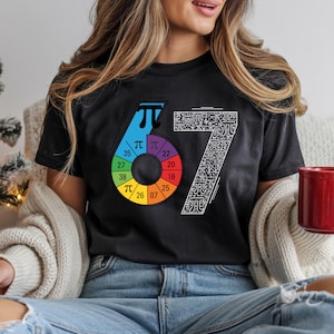 May include: Black t-shirt featuring a colorful graphic design with the numbers "67" and a pie chart with numbers and the pi symbol. The "6" is a gradient of blue, purple, and green. The "7" is white with a detailed pattern.