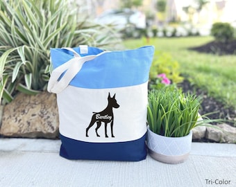May include: A blue and white canvas tote bag with a black silhouette of a dog and the name "Bartley" printed on it. The bag has a blue and white striped design and a blue bottom.