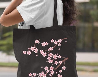 Peut inclure: Sac fourre-tout noir orné d'une branche de fleurs de cerisier roses. Les fleurs roses sont détaillées sur un fond sombre. Le sac est doté de sangles noires.