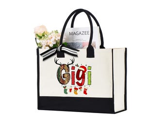 Peut inclure: Un sac fourre-tout en toile blanche avec des poignées noires et un panneau inférieur noir. Le sac porte le nom "Gigi" dans un design de Noël festif, avec des bois de cerf, un bonnet de Père Noël et des bas suspendus. Le sac est rempli de fleurs et d'un magazine.