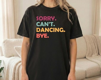 Peut inclure: T-shirt noir avec l'inscription "SORRY. CAN'T. DANCING. BYE." en lettres colorées. Le t-shirt est de style décontracté, adapté au quotidien. Le texte est en rose, bleu sarcelle, jaune et rouge.