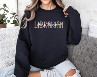 May include: A black sweatshirt with the word "Librarian" in a multi-colored font, with "Mrs. Beautiful" in a cursive font underneath. The sweatshirt is a crew neck style.