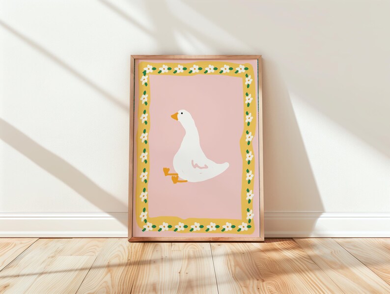 May include: A framed art print featuring a whimsical illustration of a white goose with yellow feet and beak, set against a pink background. The artwork is framed with a yellow border adorned with white flowers, creating a cheerful and decorative piece.