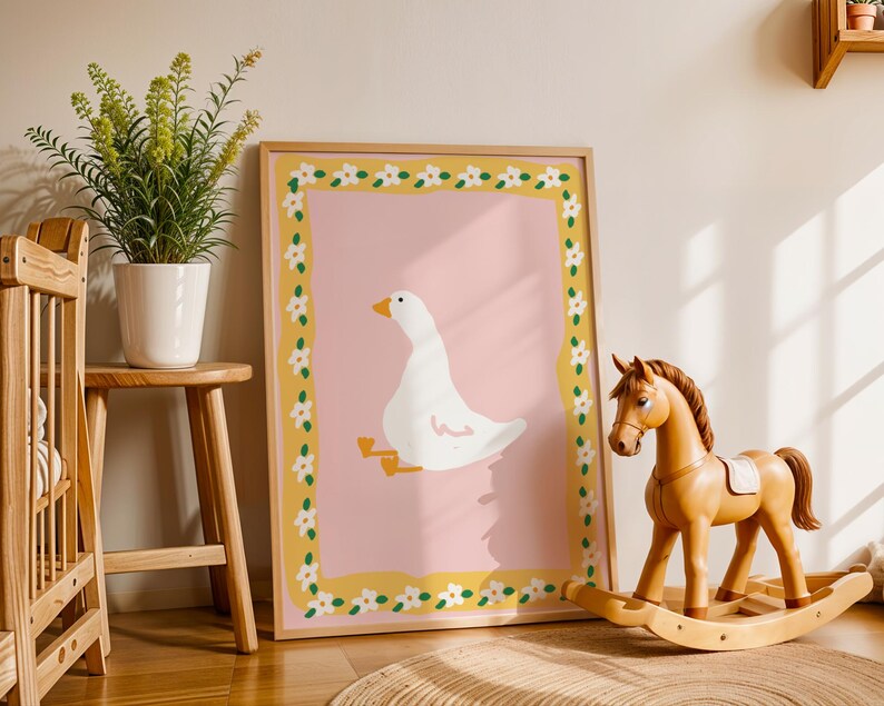 May include: A framed art print featuring a white goose illustration on a pink background, framed with a yellow border adorned with white flowers. A wooden rocking horse and a potted plant are in the foreground, creating a nursery theme.