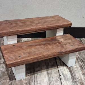 May include: A white ceramic mug with a black handle and the text "But First, Coffee" in a bold, black font. The mug is set against a blurred background, suggesting a cozy setting.