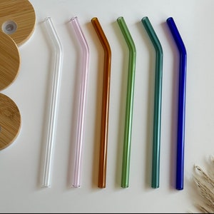 May include: Set of six glass drinking straws in various colors, including clear, purple, orange, green, blue, and dark blue. The straws are all bent and have a smooth finish.