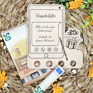 Könnte beinhalten: Eine Holzkarte in Form eines Telefons mit der Aufschrift "Wunscherfüller" und "Alles Liebe zum Geburtstag! Erfulle dir deinen Wunsch". Die Karte hat einen Schlitz für eine Geschenkkarte oder Geld und eine kleine Geschenkbox mit einem Sternenausbruch-Design.