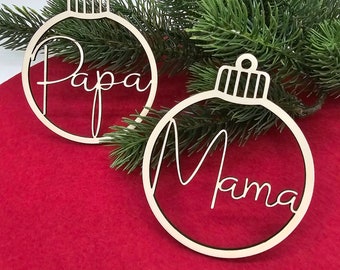 Könnte beinhalten: Zwei hölzerne Weihnachtskugeln in Form einer Kugel mit den Worten "Papa" und "Mama" in kursivschrift.