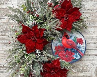 May include: A Christmas wreath with red poinsettia flowers, green pine branches, and a red cardinal bird on a blue and white plate.