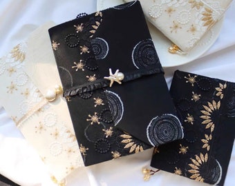 May include: Three fabric-covered journals with gold and white embroidery. The journals are decorated with lace and have a pearl-like embellishment. The text "Judy" is visible in the top left corner of the image.