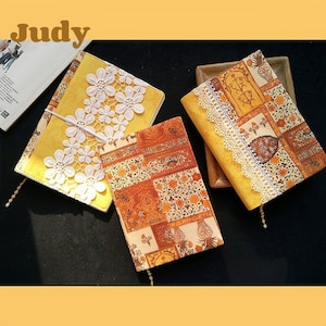 May include: Three yellow book covers with different designs. One cover features a white lace overlay, another has a floral pattern, and the third has a geometric pattern. All covers have a yellow background.