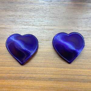 May include: Two purple heart-shaped objects on a wood surface.