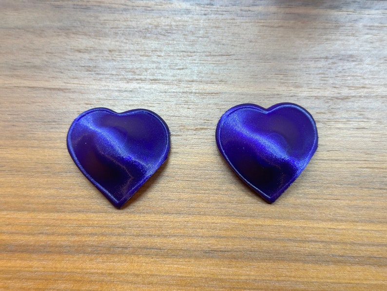 May include: Two purple heart-shaped objects on a wood surface.