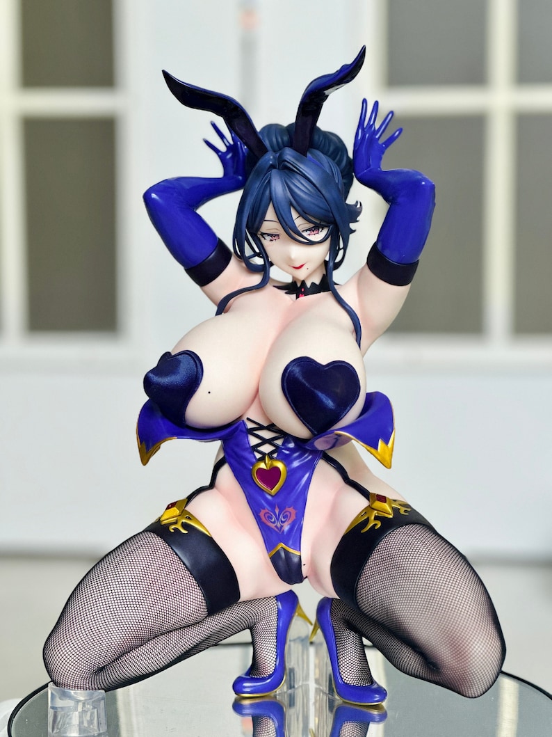 May include: A figure of a woman wearing a blue and purple bunny costume with a heart-shaped chest piece. The figure is kneeling with her hands on her head and her legs spread apart. She is wearing black fishnet stockings and blue high heels.