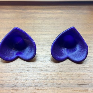May include: Two heart-shaped objects made of a dark blue material. The objects are hollow and have a smooth, slightly textured surface.