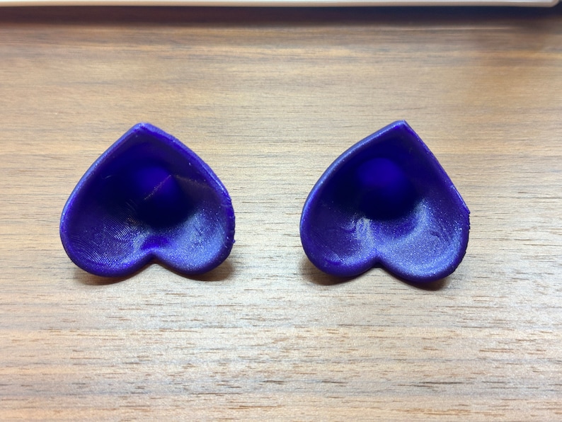 May include: Two heart-shaped objects made of a dark blue material. The objects are hollow and have a smooth, slightly textured surface.