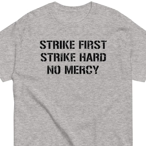 May include: Gray t-shirt with the text "Strike First Strike Hard No Mercy" printed in black.