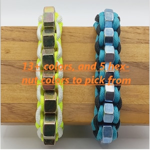 May include: Two paracord bracelets with metal hex nuts. The bracelet on the left has a white and neon yellow paracord. The bracelet on the right has a black and teal paracord.  "13+ colors, and 5 hex-nut colors to pick from"