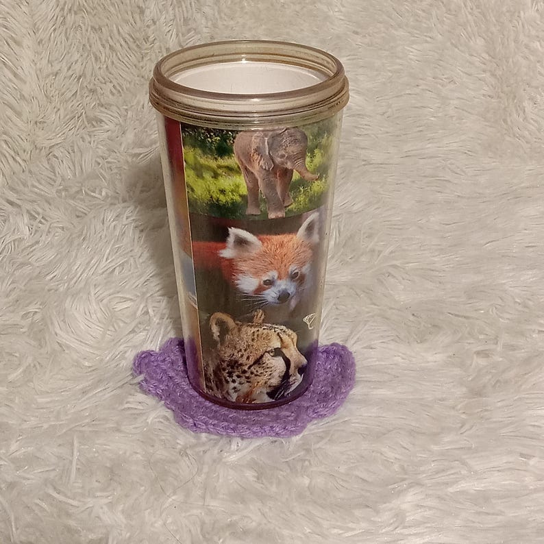 K&ouml;nnte beinhalten: Ein durchsichtiger Plastikbecher mit einem lila geh&auml;kelten Untersetzer. Der Becher hat ein Design mit einem Elefanten, einem Roten Panda und einem Geparden.