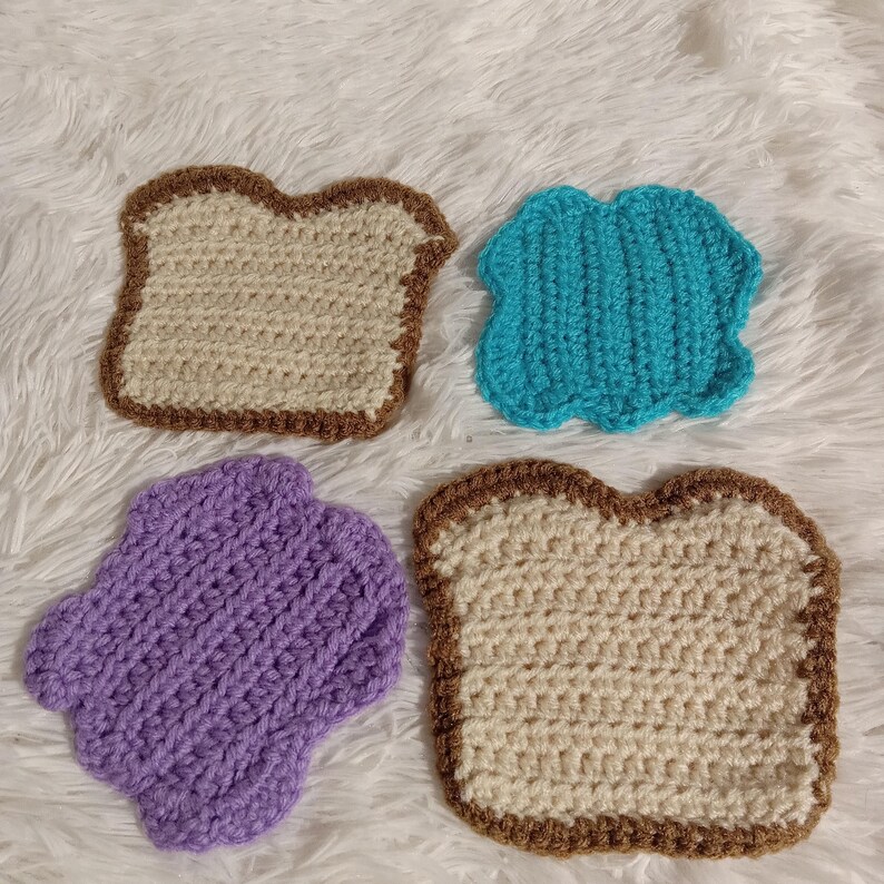 K&ouml;nnte beinhalten: Vier geh&auml;kelte Lebensmittelst&uuml;cke, darunter zwei Brotst&uuml;cke, eine lila Gelee und eine blaue Gelee.