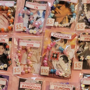 May include: A collection of colorful beaded bracelets with different member names from the K-pop group Stray Kids. Each bracelet is displayed on a card with the member's name and a price tag. The prices range from $5 to $10.