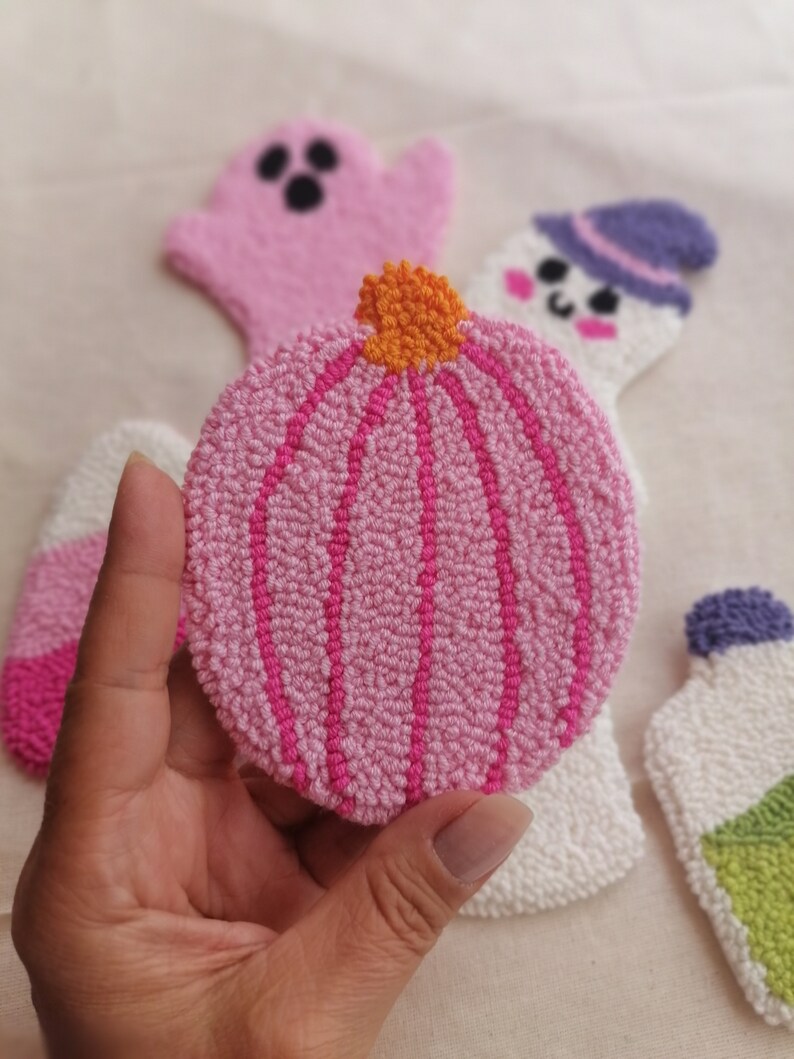 K&ouml;nnte beinhalten: Ein rosa-orangener Filz-K&uuml;rbis mit Stiel. Der K&uuml;rbis ist umgeben von anderen Filz-Halloween-Dekorationen, darunter ein Geist, ein Schneemann und eine Flasche.
