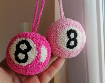 Può includere: Due ornamenti a forma di 8-ball in crochet rosa con cuciture nere e dettagli bianchi.